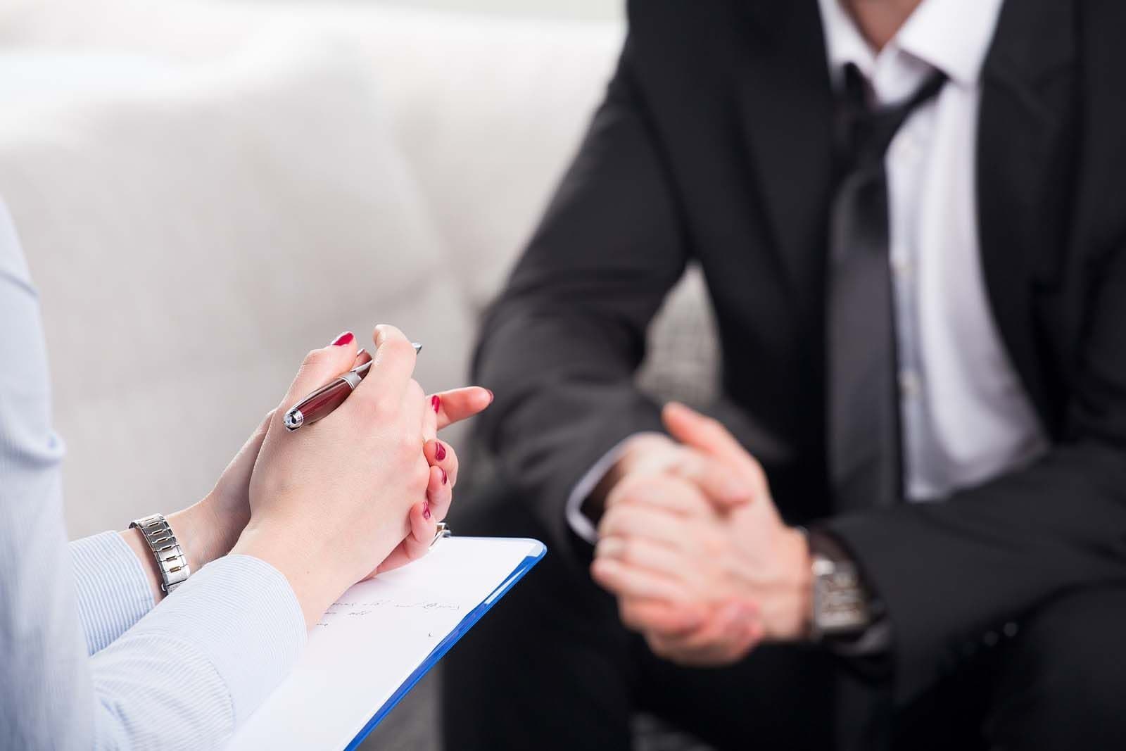 A counseling session in progress with a clipboard and clasped hands