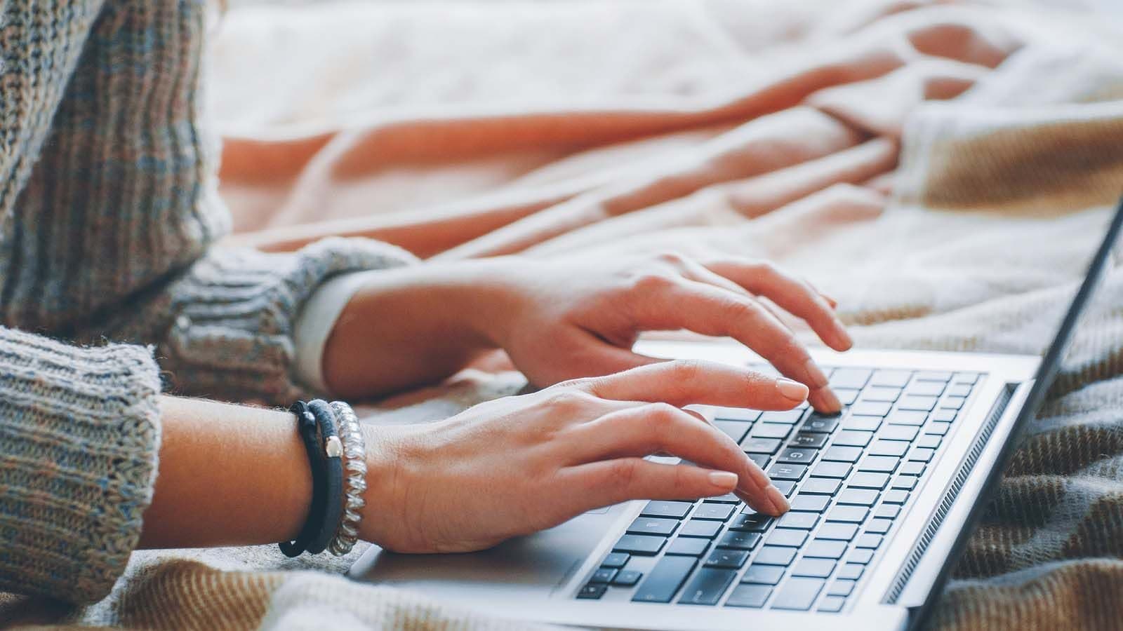 A person in a cozy sweater typing on a laptop at home during an online therapy session