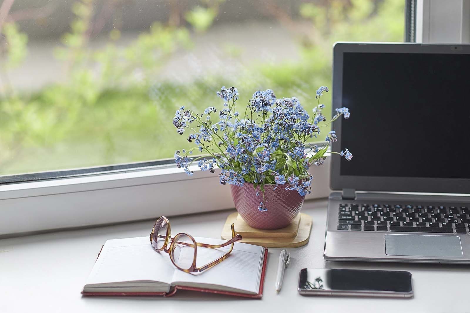 A desk with a notebook, glasses and laptop set up for research