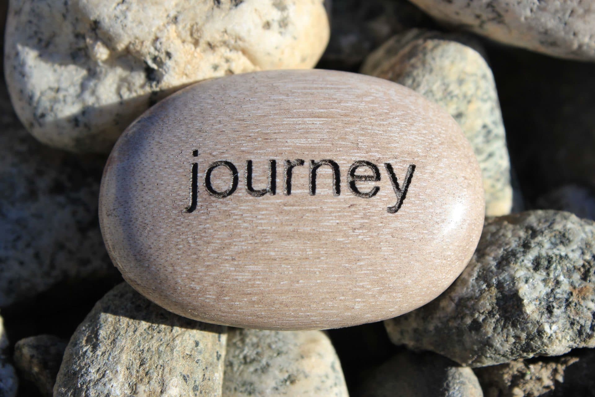 A smooth stone engraved with the word journey resting among river rocks