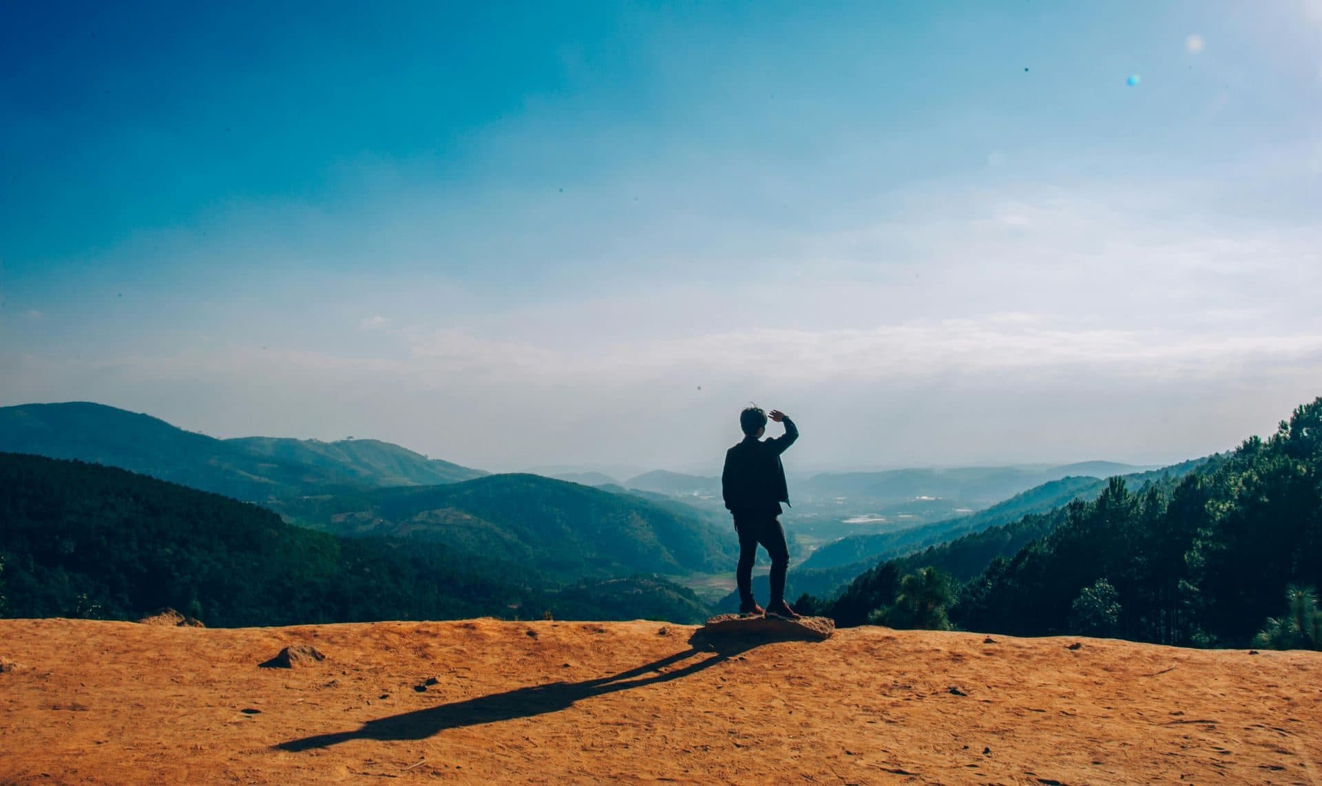 A man standing on a cliff overlooking a wide valley at sunrise, representing hope after depression