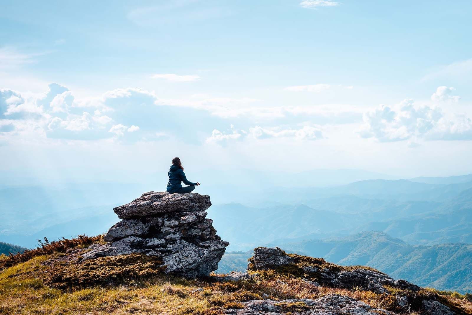 A person sitting calmly on a rock overlooking mountains, representing relief from anxiety