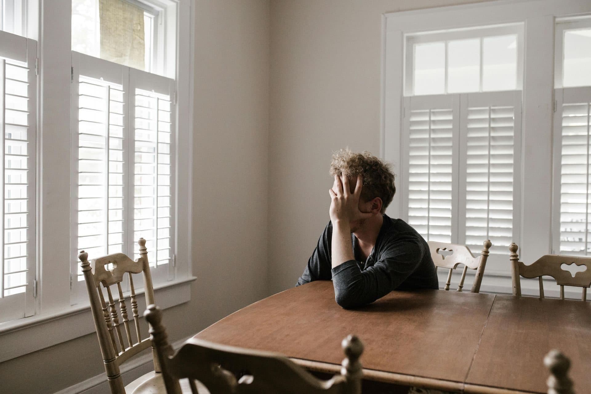 A person sitting alone at a dining table with their head in their hand, processing the aftermath of divorce
