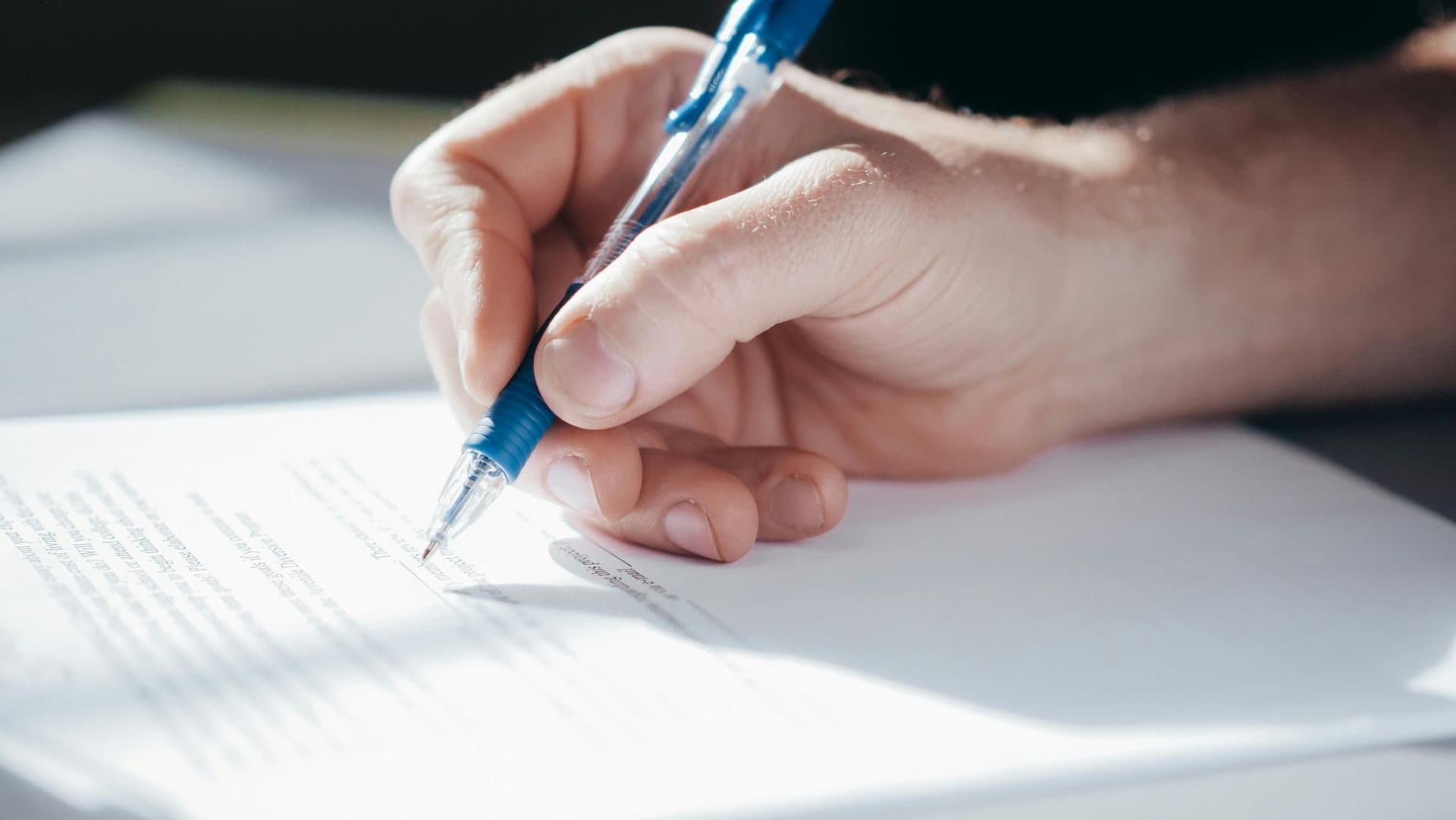 A hand signing a document with a pen