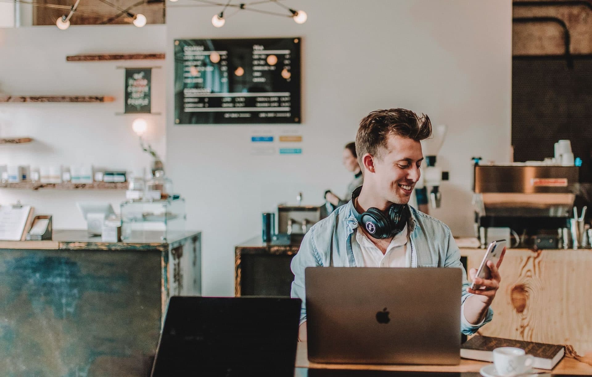 A smiling man sitting at a cafe table with a laptop, representing confidence after individual therapy