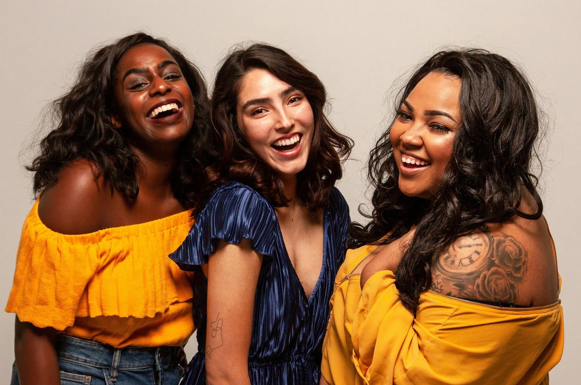 Three women laughing together outdoors, representing connection and wellness